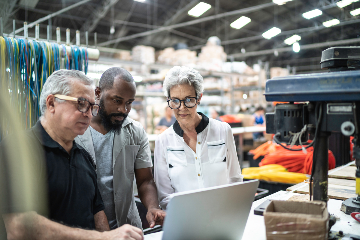 Group of three workers in a warehouse setting crowding around a laptop