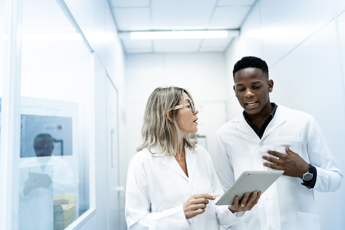 Two scientists walking down a hallway. One is holding a tablet while the other one is using his hands as he explains