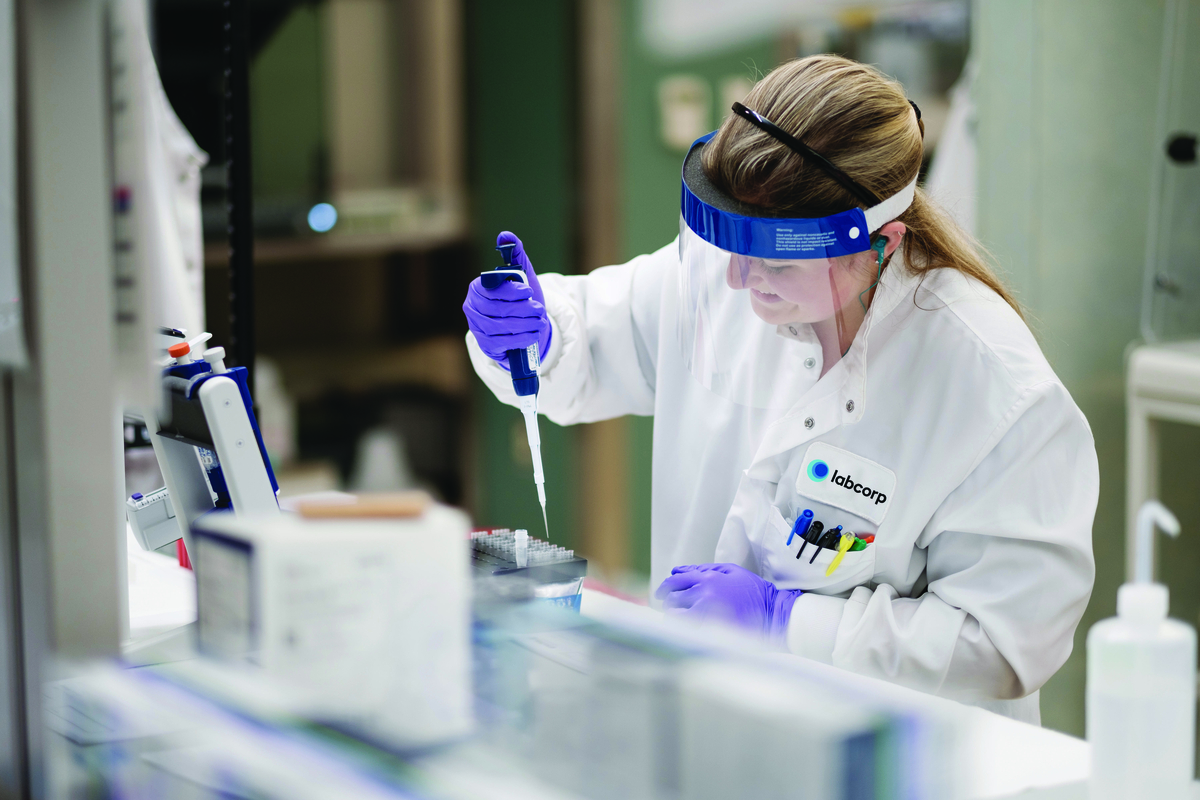 Labcorp lab worker holding a pipette. She is wearing a face guard and gloves