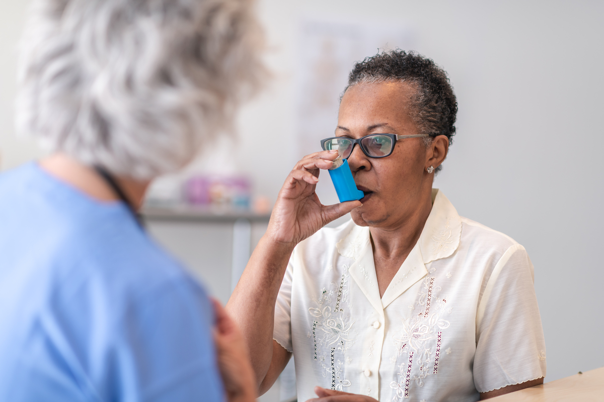 Older patient taking a puff from an inhaler with provider in the foreground