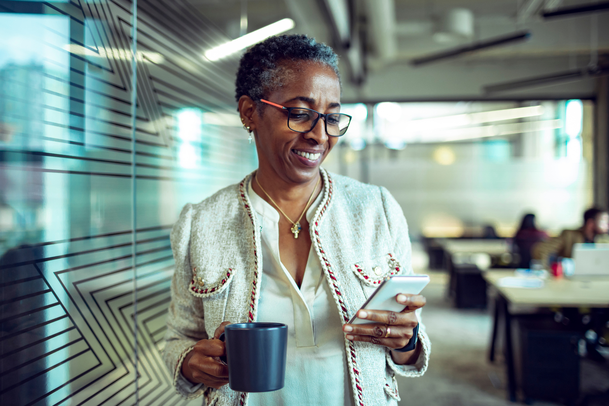 1281124021 Close up of a senior businesswoman using a phone while having coffee in the office
